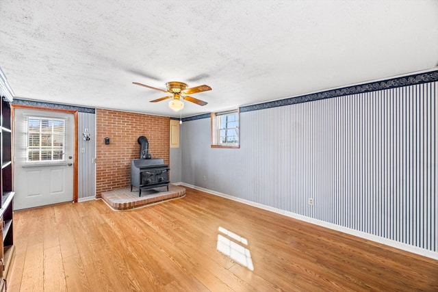 unfurnished living room with ceiling fan, a wood stove, a textured ceiling, and light wood-type flooring