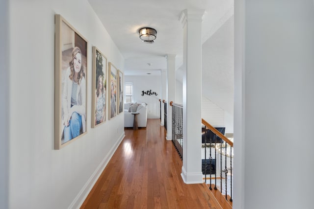 hallway featuring baseboards, an upstairs landing, decorative columns, and wood-type flooring