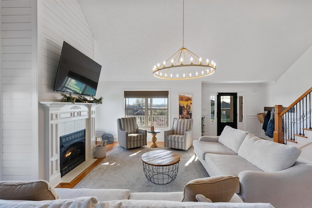 living area with a tile fireplace, a chandelier, stairs, wood finished floors, and lofted ceiling