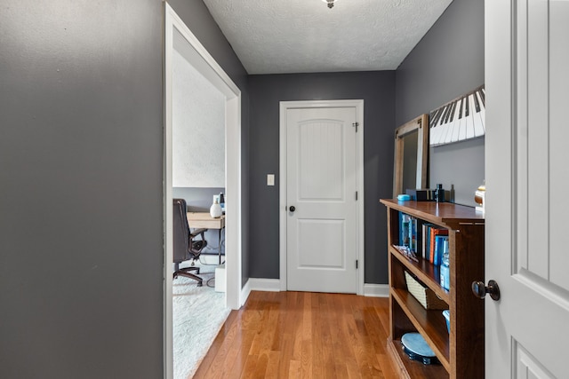 hallway with baseboards, wood finished floors, and a textured ceiling