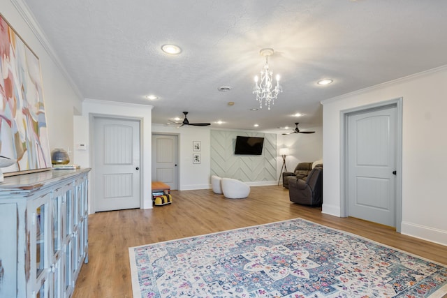 sitting room with a textured ceiling, light wood-style flooring, crown molding, and ceiling fan with notable chandelier