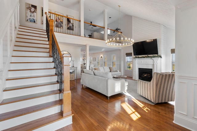living area featuring decorative columns, high vaulted ceiling, stairway, a fireplace, and hardwood / wood-style floors