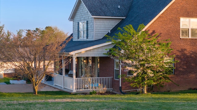 view of home's exterior featuring brick siding, a sunroom, roof with shingles, and a lawn