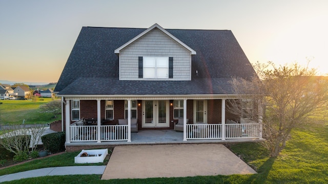 view of front of house featuring covered porch, brick siding, french doors, and roof with shingles