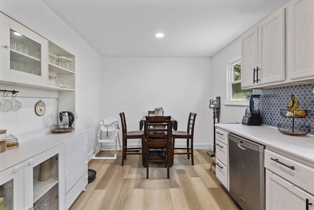 kitchen with light countertops, stainless steel dishwasher, light wood-style floors, glass insert cabinets, and tasteful backsplash