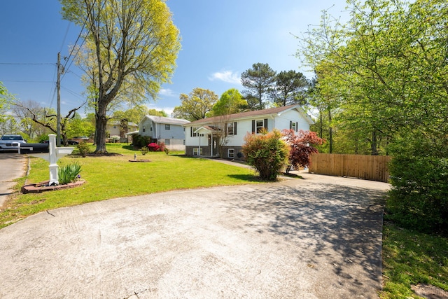 raised ranch featuring a front lawn, driveway, and fence