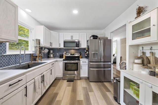 kitchen with tasteful backsplash, a sink, light countertops, light wood-style flooring, and appliances with stainless steel finishes