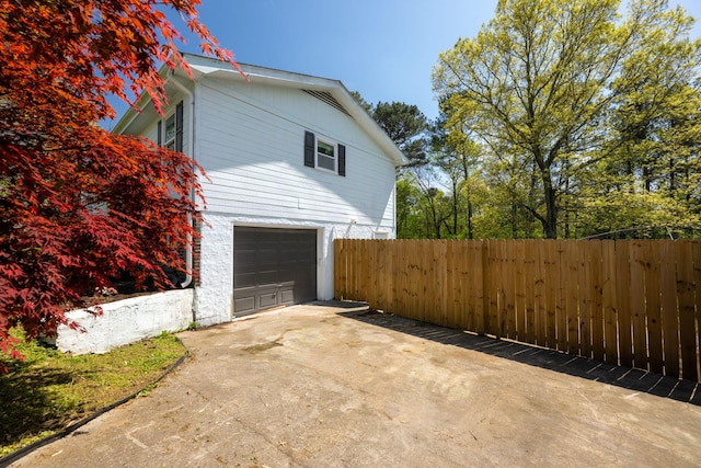 view of side of property featuring fence, an attached garage, and concrete driveway