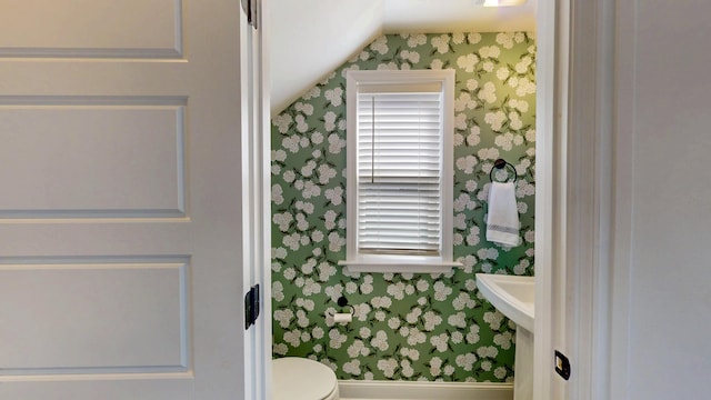 half bathroom with wallpapered walls, toilet, and lofted ceiling