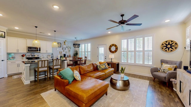living area with wood finished floors, ornamental molding, a ceiling fan, and recessed lighting