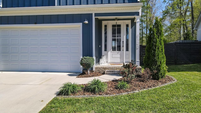 view of exterior entry featuring a yard, a garage, board and batten siding, fence, and concrete driveway