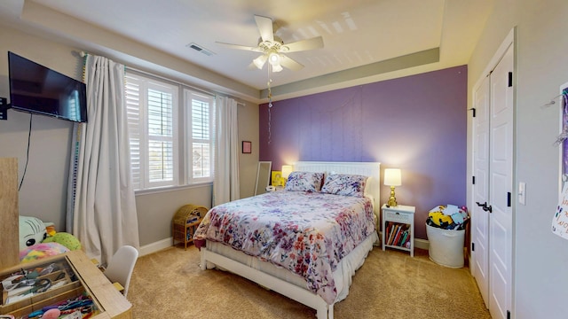 bedroom featuring baseboards, a raised ceiling, visible vents, ceiling fan, and light colored carpet