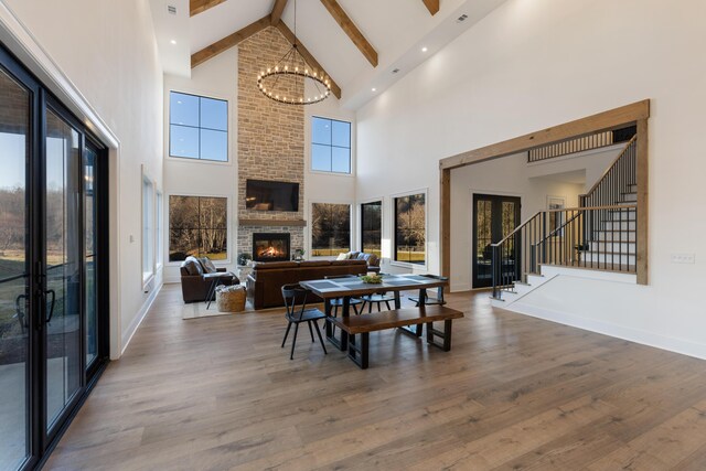 dining room featuring a brick fireplace, stairway, wood finished floors, and beamed ceiling