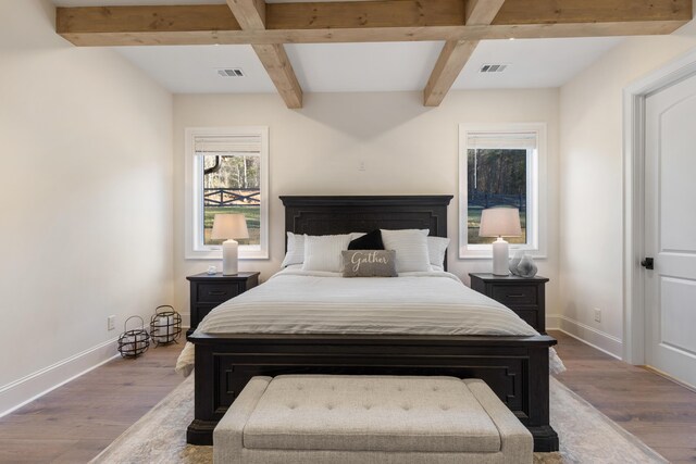 bedroom with wood finished floors, beamed ceiling, visible vents, and baseboards