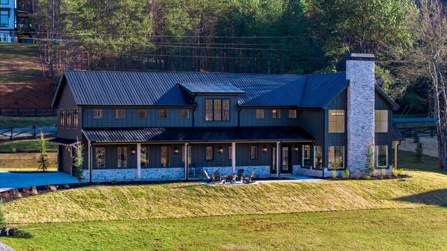 rear view of property with metal roof, a lawn, stone siding, and a chimney