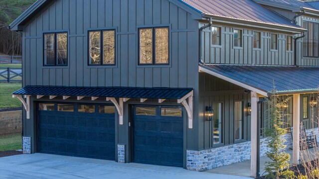 view of front of house with driveway, stone siding, board and batten siding, an attached garage, and metal roof