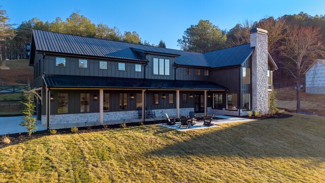 rear view of house featuring an outdoor fire pit, a chimney, stone siding, a lawn, and metal roof