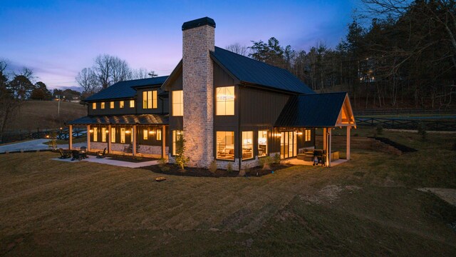 back of house featuring metal roof, stone siding, a lawn, and a chimney