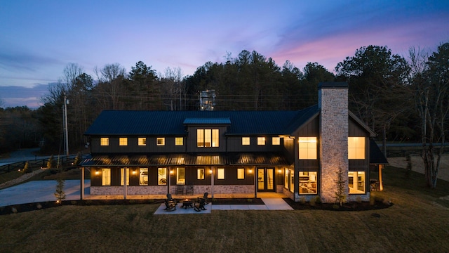 rear view of house with a standing seam roof, a yard, metal roof, a chimney, and a patio area