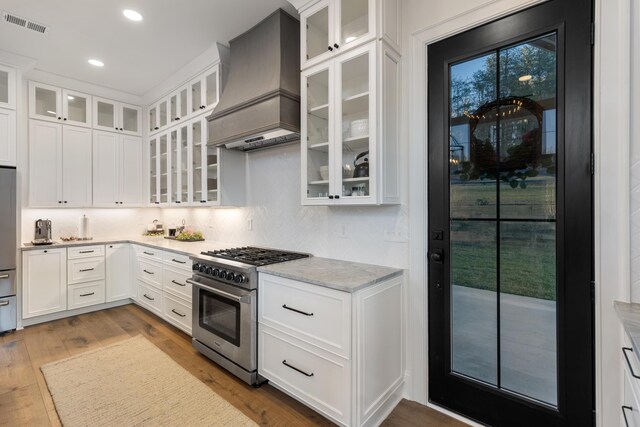 kitchen featuring visible vents, custom range hood, wood finished floors, white cabinets, and stainless steel appliances