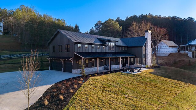 view of front of property with concrete driveway, a front yard, a chimney, metal roof, and a garage