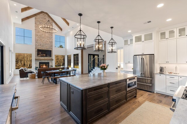 kitchen featuring wood finished floors, high quality fridge, white cabinets, a brick fireplace, and a chandelier