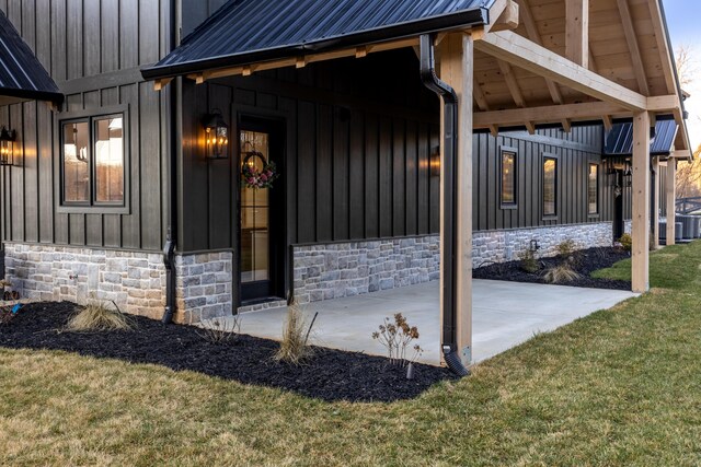 view of exterior entry with a lawn, board and batten siding, stone siding, and metal roof