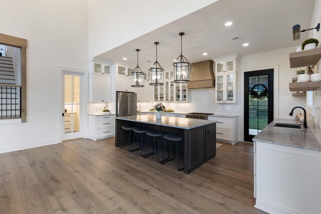 kitchen featuring open shelves, premium range hood, a breakfast bar area, high quality fridge, and a sink