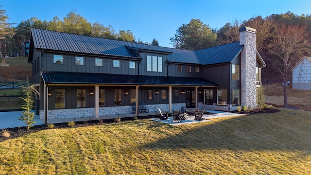 back of house featuring a fire pit, a chimney, metal roof, a yard, and stone siding