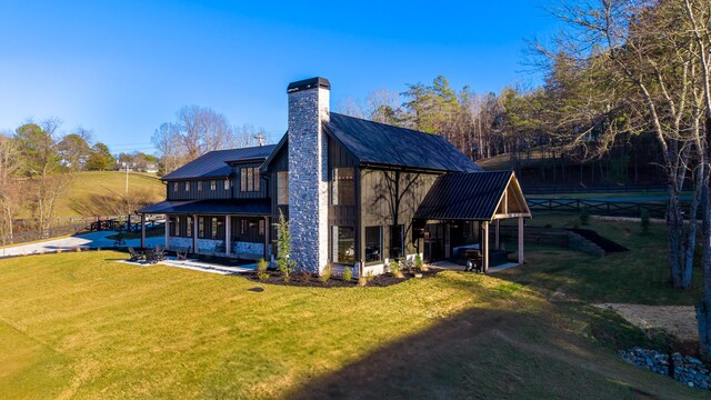 rear view of property featuring metal roof, a patio, a lawn, and a chimney