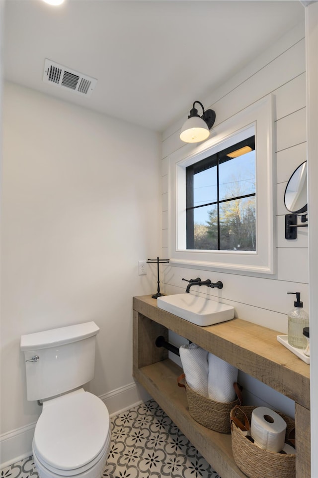 half bathroom featuring a sink, visible vents, baseboards, and toilet