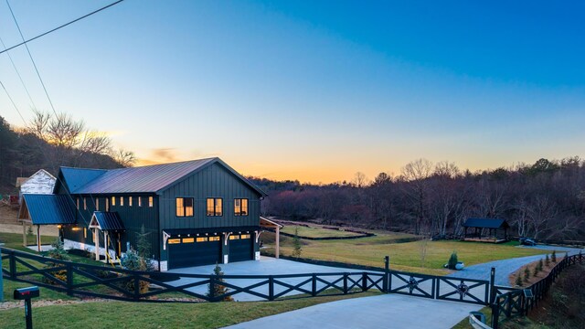 rear view of property featuring driveway, fence, board and batten siding, an attached garage, and metal roof