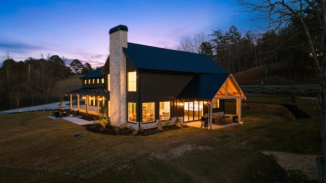 back of property at dusk featuring a patio area, a yard, metal roof, and a chimney