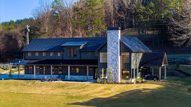 back of house featuring a yard, metal roof, a chimney, and a sunroom