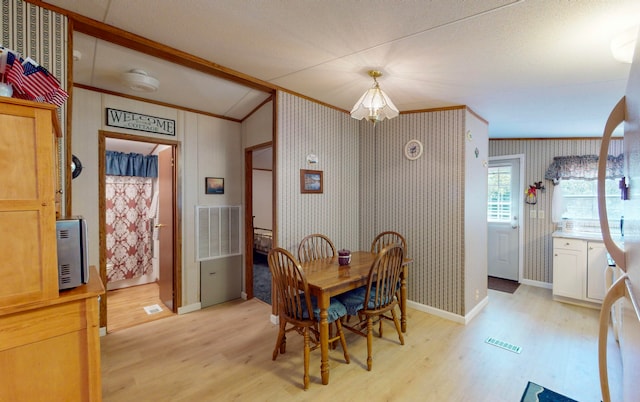 dining area featuring light wood-type flooring, an inviting chandelier, lofted ceiling, and crown molding