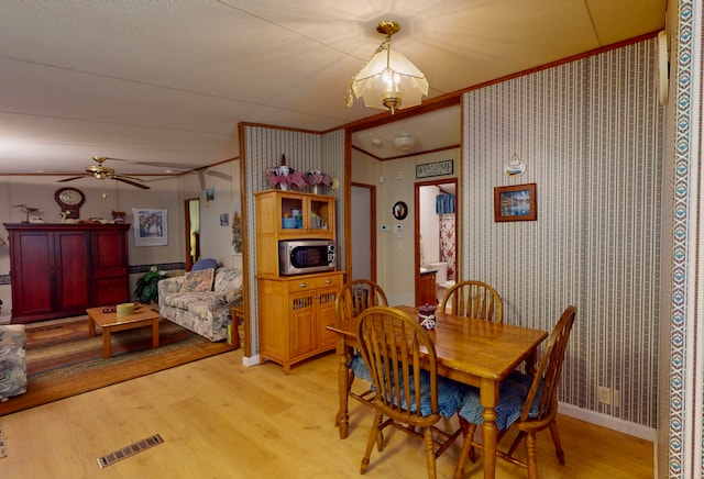 dining room featuring ornamental molding, ceiling fan with notable chandelier, and light wood-type flooring