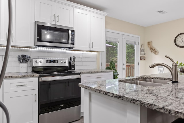 kitchen with light stone countertops, appliances with stainless steel finishes, french doors, sink, and white cabinetry