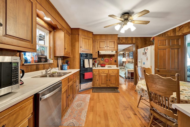 kitchen with sink, stainless steel appliances, ornamental molding, light hardwood / wood-style floors, and wood walls