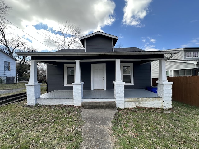 bungalow-style home with covered porch, a front lawn, and fence