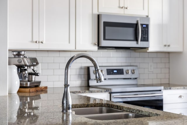 kitchen with a sink, white cabinetry, appliances with stainless steel finishes, light stone countertops, and tasteful backsplash