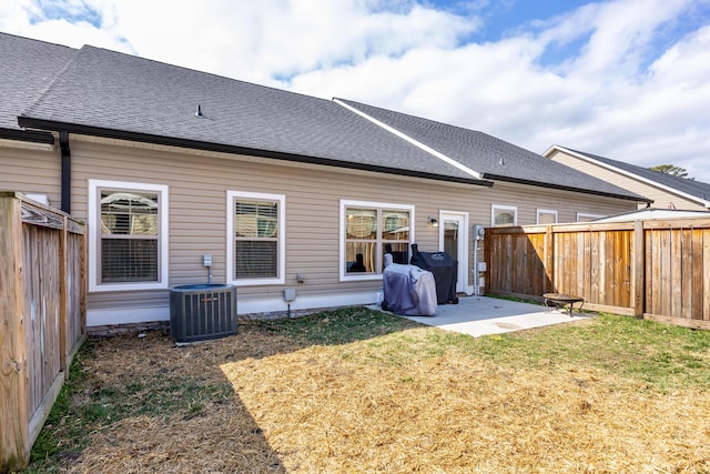 rear view of property with a lawn, a patio, roof with shingles, fence, and central AC