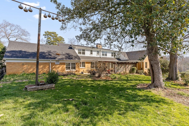 rear view of house featuring stone siding, a chimney, a yard, and a shingled roof