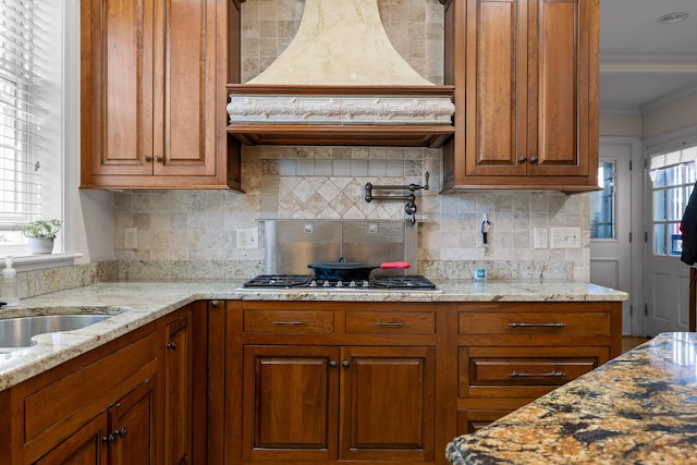 kitchen with crown molding, brown cabinets, premium range hood, and stainless steel gas cooktop