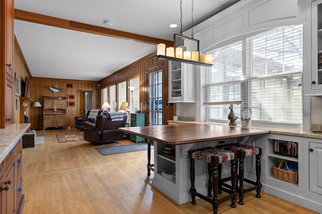 dining room with light wood-type flooring, beamed ceiling, wood walls, and crown molding