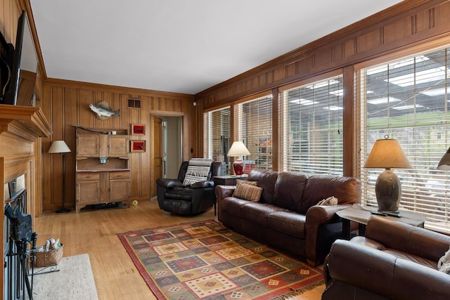 living room featuring wooden walls, light wood-style flooring, visible vents, and ornamental molding