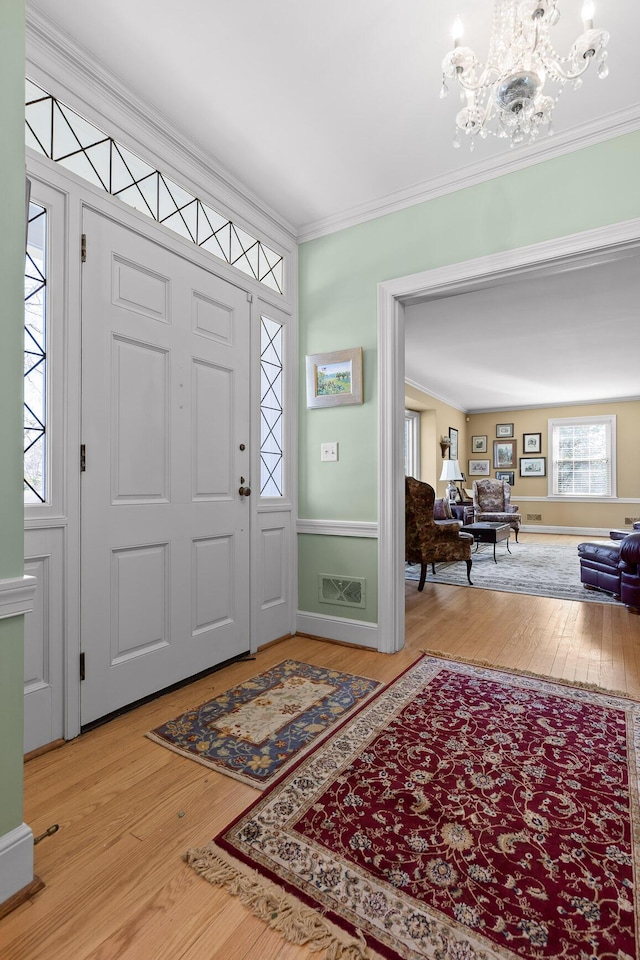 entrance foyer with visible vents, an inviting chandelier, wood finished floors, and crown molding