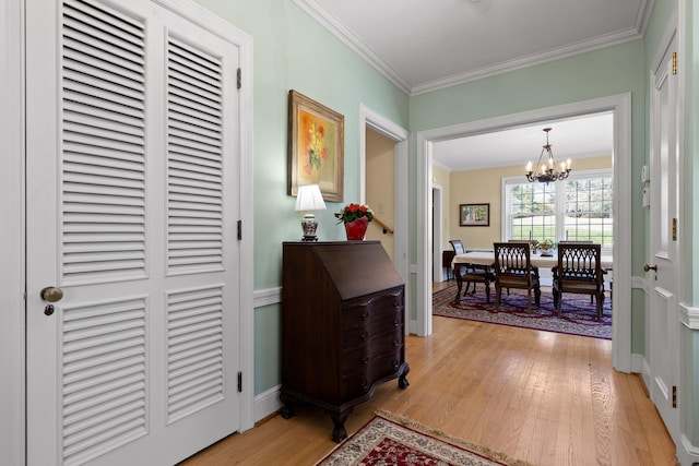 hall featuring light wood-type flooring, baseboards, a notable chandelier, and ornamental molding