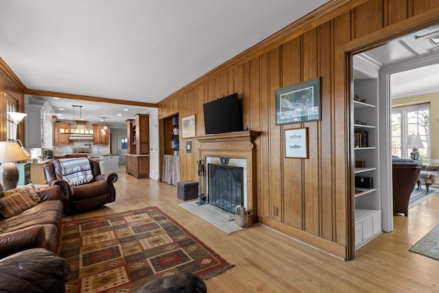 living area with a fireplace with flush hearth, built in features, wooden walls, light wood-style floors, and crown molding