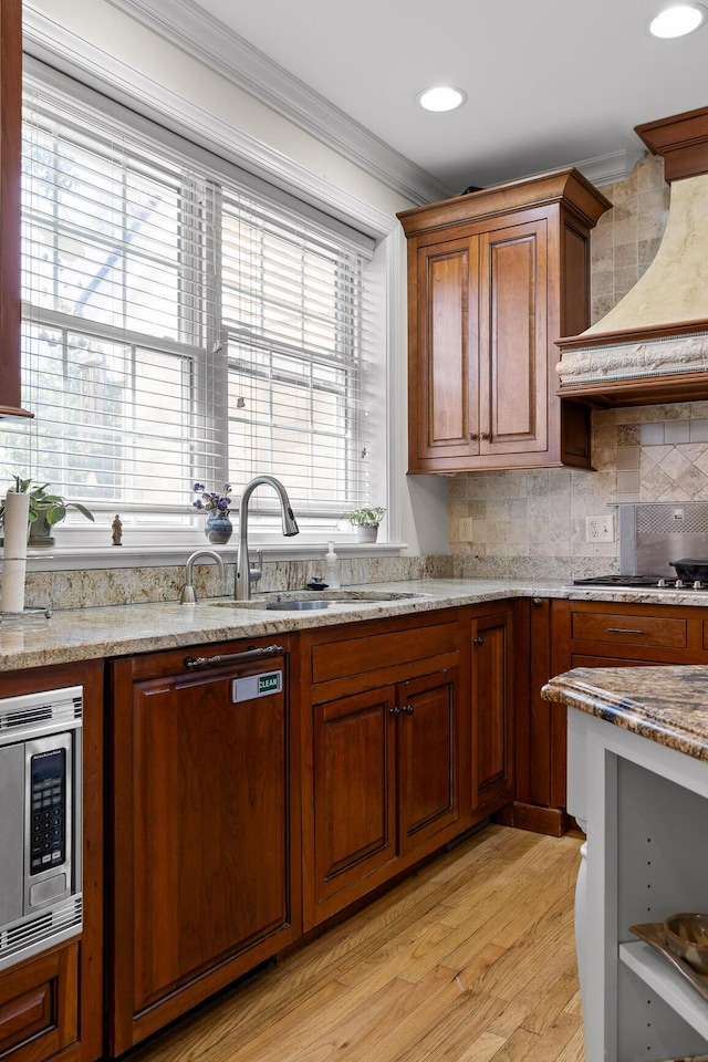 kitchen with tasteful backsplash, custom range hood, ornamental molding, appliances with stainless steel finishes, and a sink