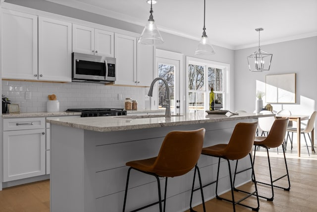 kitchen with light wood-style floors, a kitchen island with sink, stainless steel microwave, and white cabinets